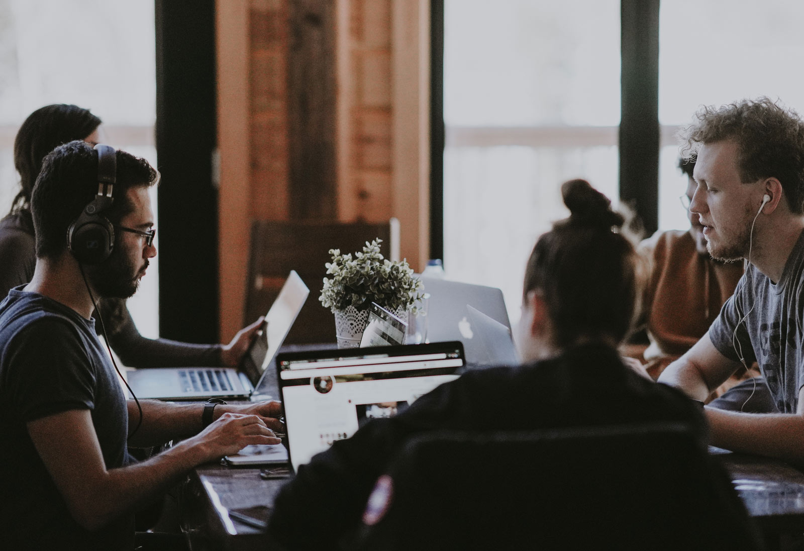 Two people sit around three laptops on a table in a co-working space.